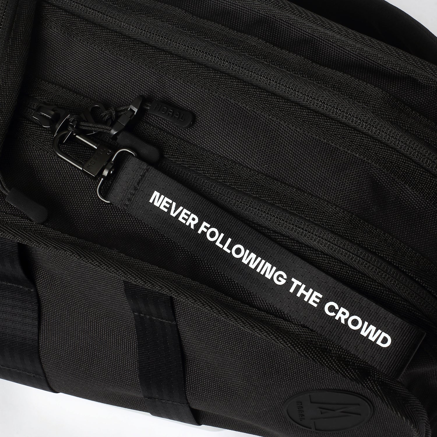 MORAL Napier Poser 運動背包大碼黑色,特寫展示品牌拉鍊與織帶掛飾,上有「NEVER FOLLOWING THE CROWD」字樣。包款細節設計強調個性與實用性。