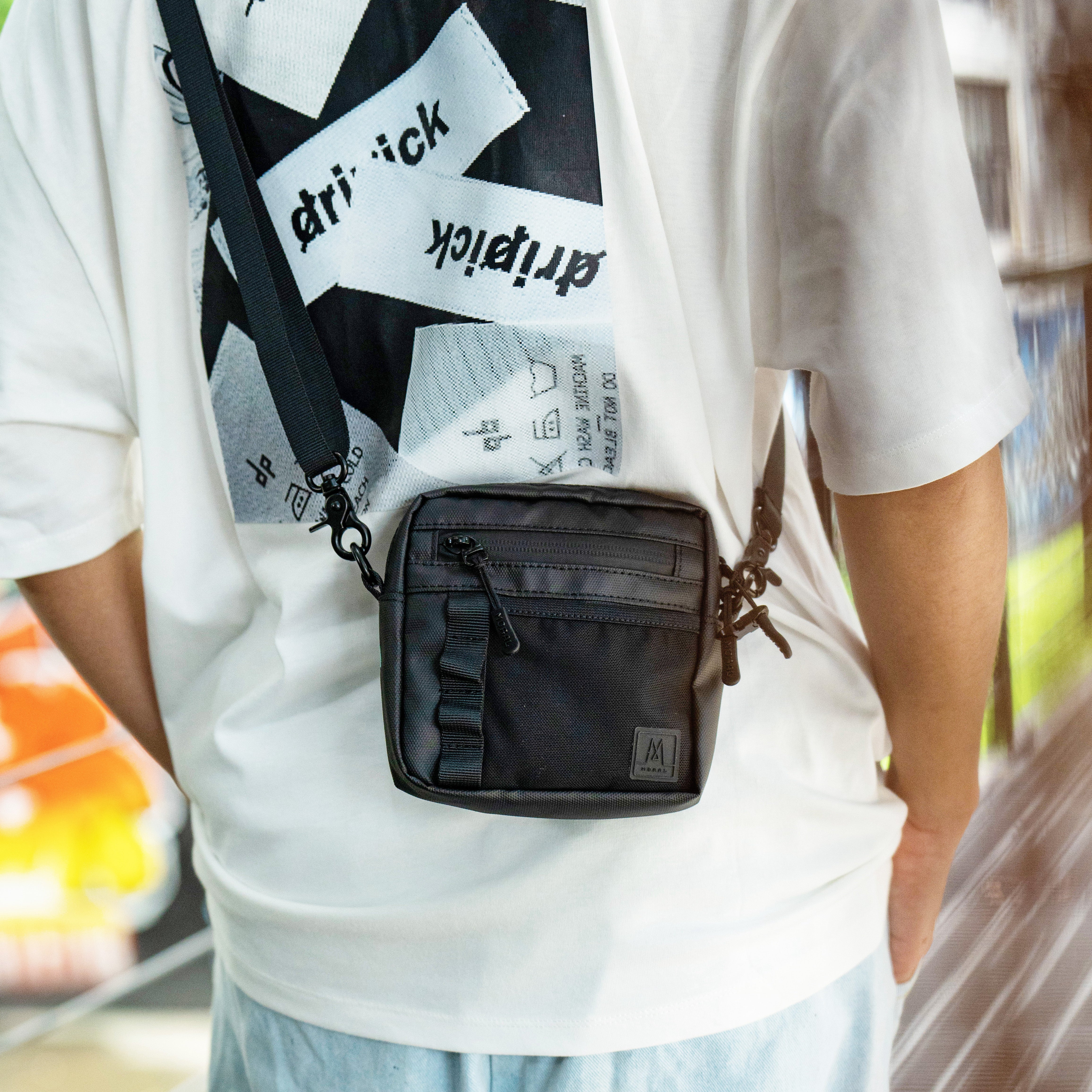 Moral Napier Cubic 輕便小側背包,突顯防水拉鏈與前方裝飾織帶細節。展現實用分隔設計與時尚外觀。