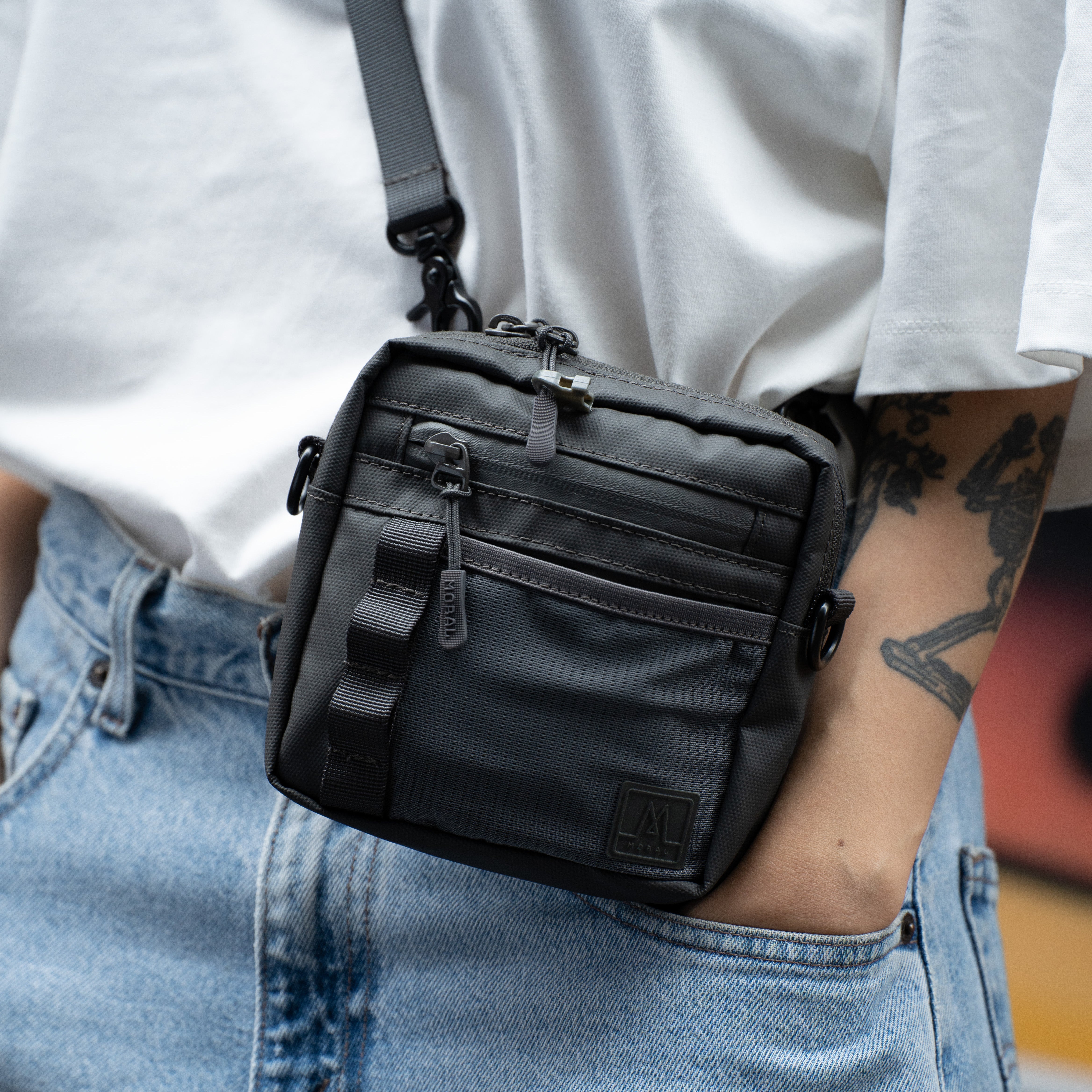 Moral Napier Cubic 輕便小側背包,突顯防水拉鏈與前方裝飾織帶細節。展現實用分隔設計與時尚外觀。